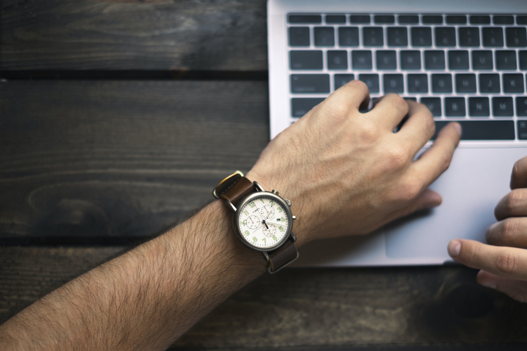 man wearing a brown watch typing on his laptop